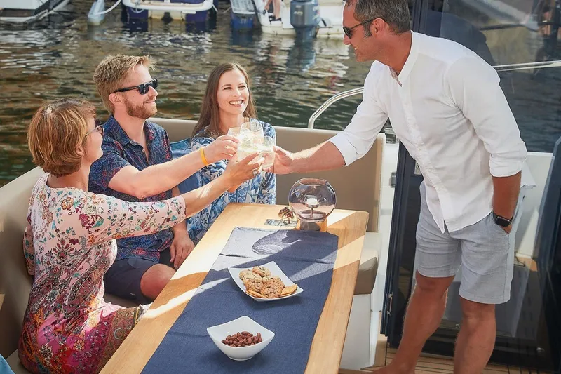 Slide: The Image of Vier Personen stoßen auf einem Boot an, während sie an einem Tisch im Freien sitzen. - 21