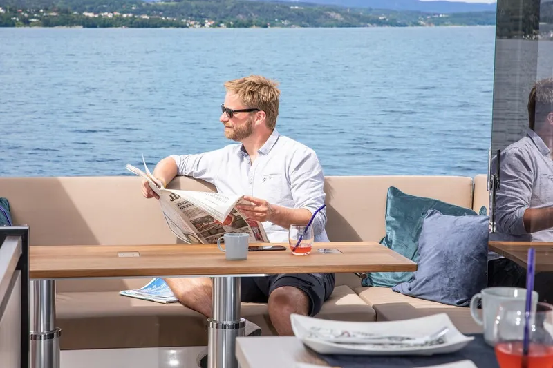 Slide: The Image of Mann liest Zeitung auf einer Sealine C390 Yacht, umgeben von Wasser und Bergen. - 15