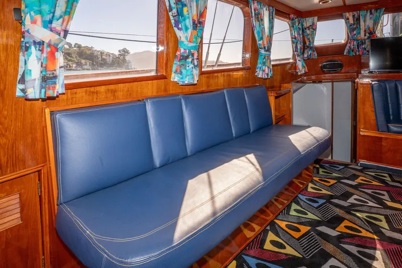 Slide: The Image of Interior of a 1981 Thackwray Motorsailor with blue seating, colorful curtains, and patterned carpet. - 115