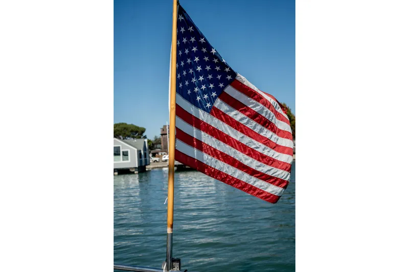 Slide: The Image of American flag on Thackwray Motorsailor, 1981, with waterfront background. - 26