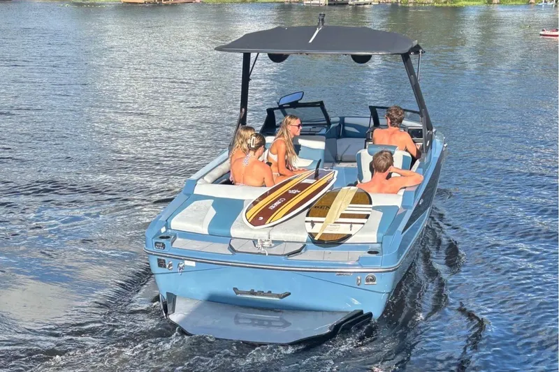 Slide: The Image of 2023 Axis T220 boat with passengers and surfboards on a sunny lake. - 2