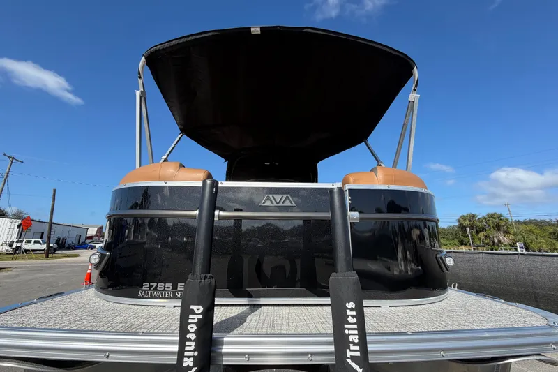Slide: The Image of 2025 Avalon Excalibur LTD Quad Lounge boat with windshield, parked on a trailer under blue sky. - 14