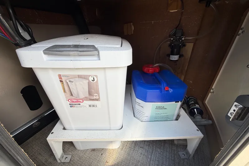 Slide: The Image of Storage compartment in 2025 Avalon Excalibur LTD boat with Sterilite container and blue tank. - 27