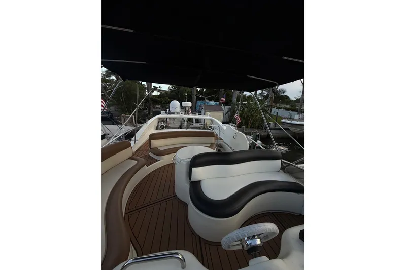 Slide: The Image of 1999 Azimut 52 yacht deck with elegant seating and steering wheel, docked near lush greenery. - 1