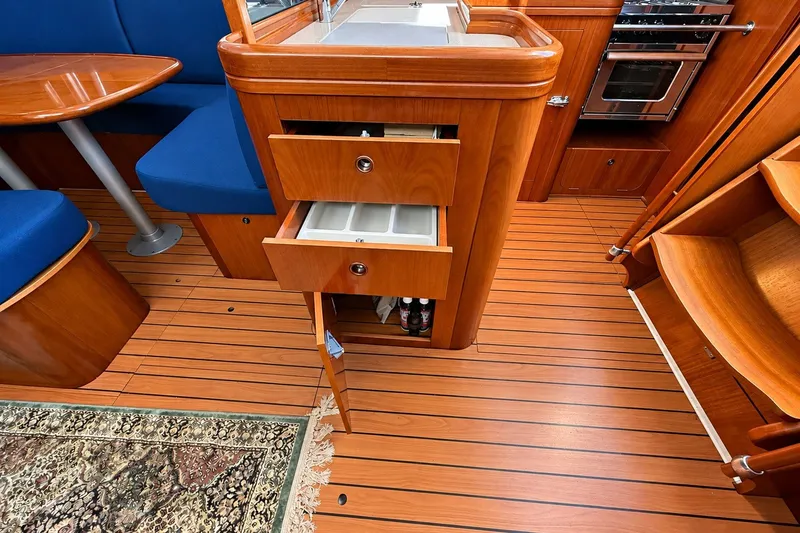 Slide: The Image of 2005 Beneteau Oceanis 473 interior with wood cabinetry, open drawers, and blue seating. - 20
