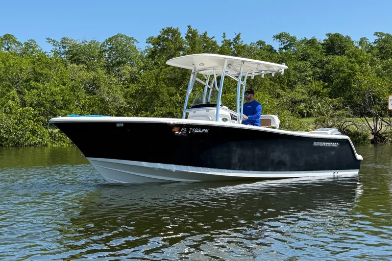 Slide: The Image of 2013 Sportsman Heritage 229 Center Console boat on calm water, surrounded by lush greenery. - 2