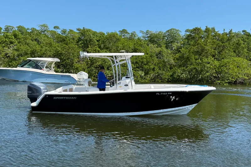 The Image of 2013 Sportsman Heritage 229 Center Console boat on calm water, surrounded by lush greenery. - 1