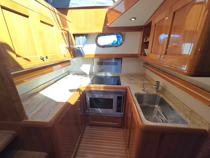 Slide: The Image of The galley of a 2010 Grand Banks SX with wooden cabinets, sink, stove, and microwave. - 33