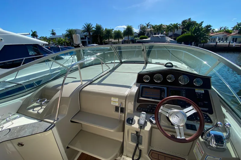 Slide: The Image of 2012 Sea Ray 330 Sundancer helm with steering wheel and control panel, docked by waterfront homes. - 24