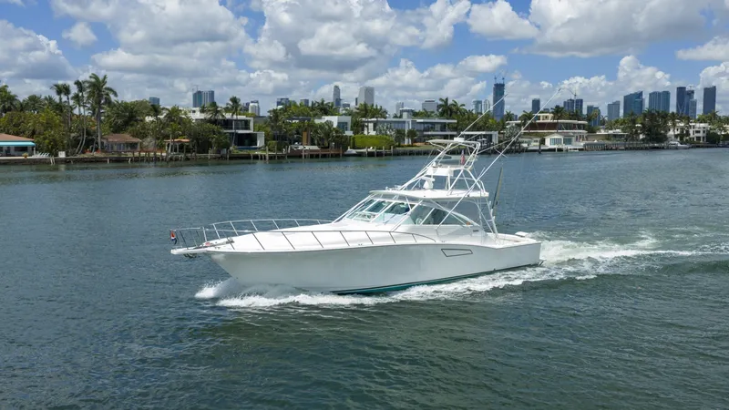 The Image of A white 2000 Cabo 45 Express cruising on a waterway, surrounded by modern buildings and palm trees. - 2