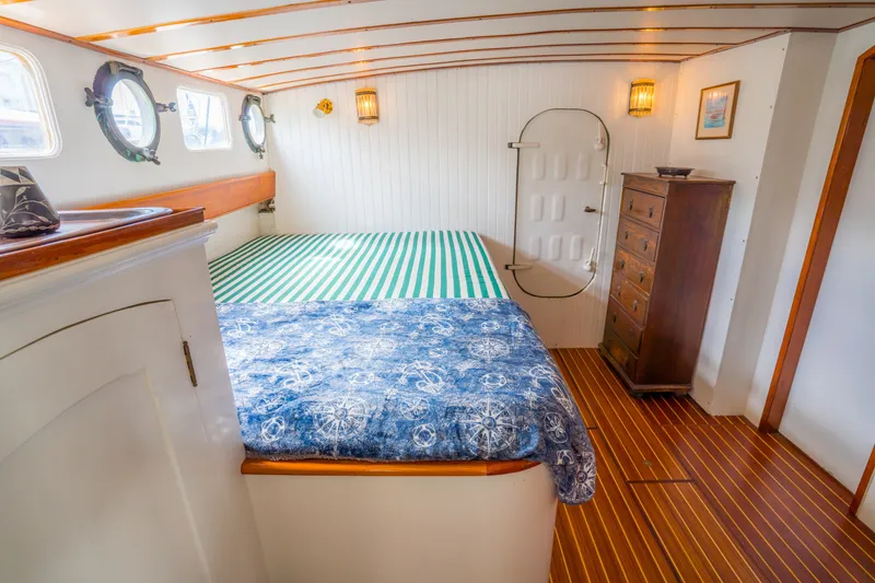Slide: The Image of 1922 Blanchard Shipyard custom boat interior with cozy cabin, striped bedding, and wooden dresser. - 53