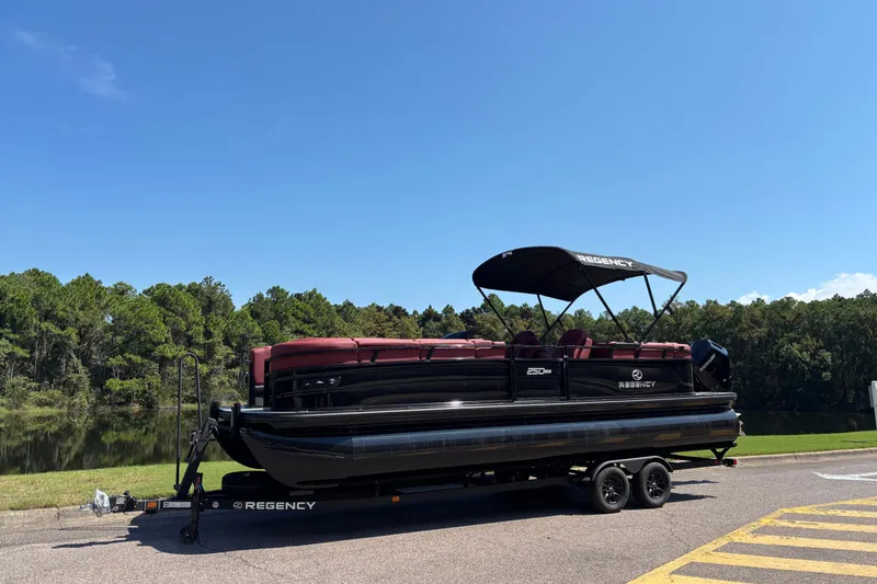 Slide: The Image of 2027 Regency R250DL3 pontoon boat on trailer by a scenic lake. - 1