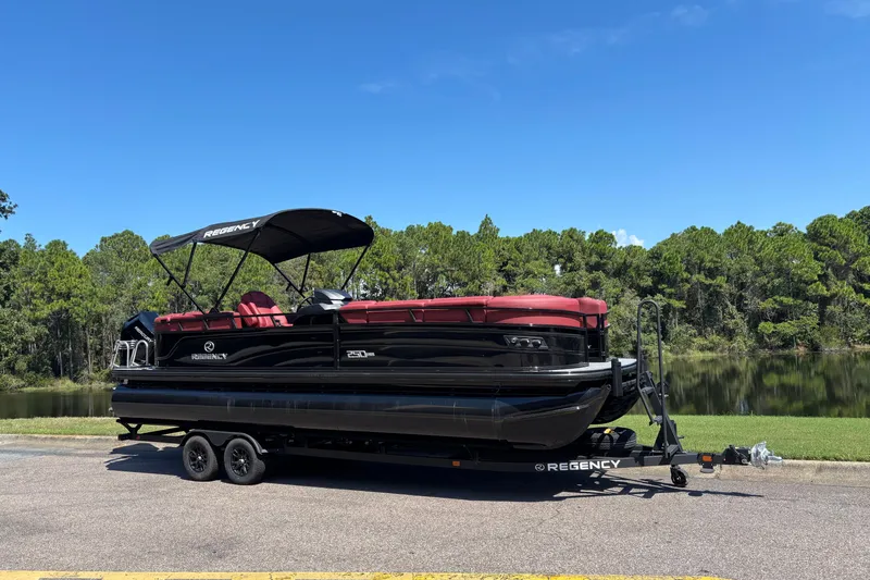 Slide: The Image of 2027 Regency R250DL3 pontoon boat on trailer, parked by a scenic lake with trees. - 12
