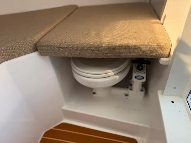 Slide: The Image of The 2024 Steiger Craft 255 Miami features a compact toilet beneath a cushioned bench seat. - 20