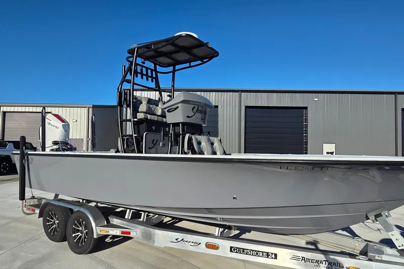 Slide: The Image of 2024 Young Boats 26 Gulfshore on trailer, parked outside industrial building under clear blue sky. - 17