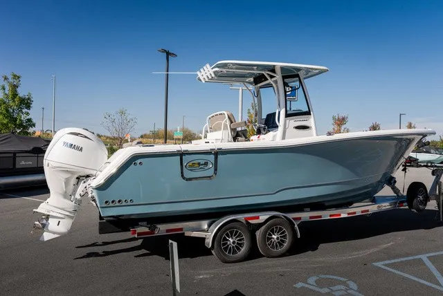 The Image of Sea Hunt Ultra 265SE 2027 on a trailer, featuring a blue hull and white outboard motor. - 0
