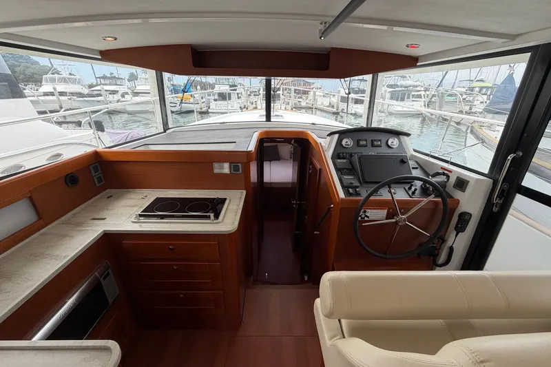 Slide: The Image of 2019 Beneteau Swift Trawler 44 interior with helm, kitchen, and marina view. - 16
