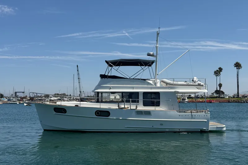 Slide: The Image of 2019 Beneteau Swift Trawler 44 cruising in a sunny harbor with palm trees in the background. - 2