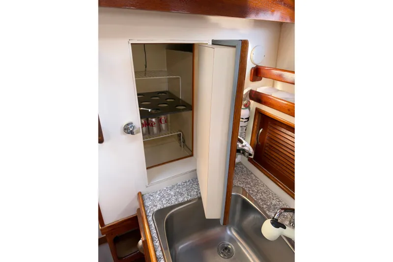 Slide: The Image of Compact kitchen area in a 1997 Covey Island Spencer Lincoln boat, featuring a small fridge and sink. - 16