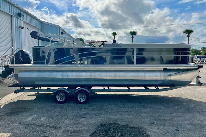 Slide: The Image of 2024 Harris Cruiser 230 pontoon boat on trailer, parked outdoors under a cloudy sky. - 16