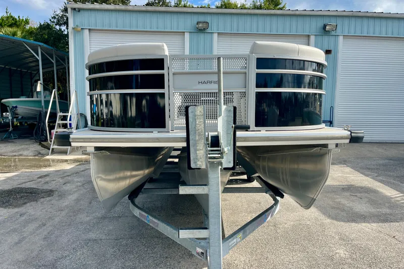 Slide: The Image of 2024 Harris Cruiser 230 pontoon boat on trailer, parked outside a storage facility. - 15