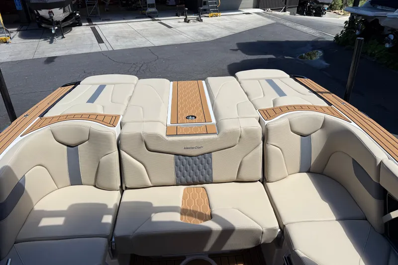 Slide: The Image of 2027 MasterCraft XT23 boat interior with beige and gray seating, docked at a marina. - 2