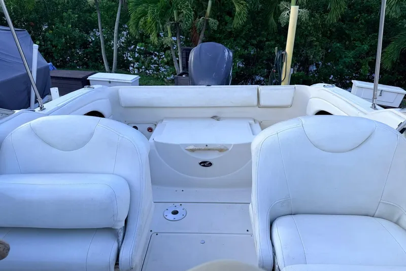 Slide: The Image of 2002 Sea Ray 225 Weekender boat interior with white seating and lush greenery background. - 6