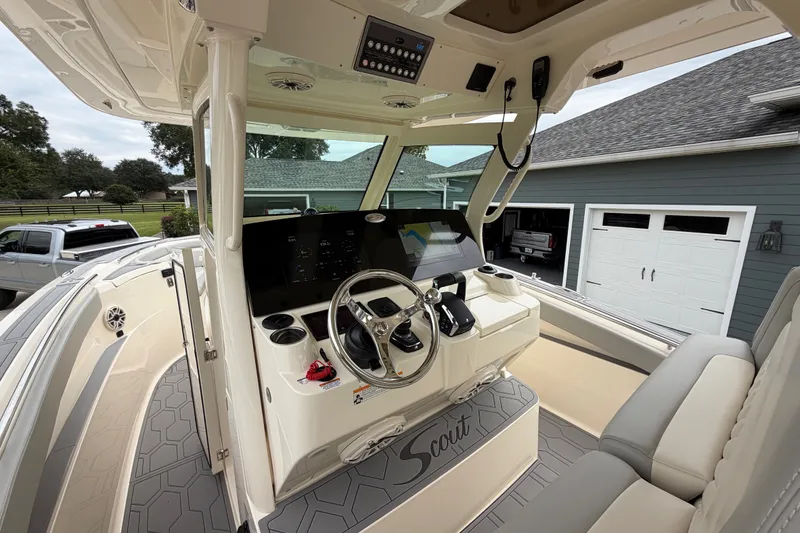 Slide: The Image of 2026 Scout 330 LXF boat cockpit with modern controls and seating, parked near a garage. - 36