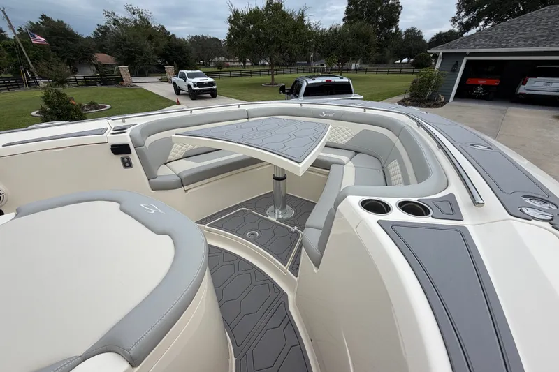 Slide: The Image of 2026 Scout 330 LXF boat interior with seating and table, parked in a driveway. - 17