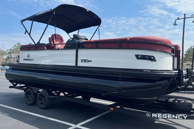 The Image of 2027 Regency 230DL3 pontoon boat with red seating, parked on a trailer. - 0