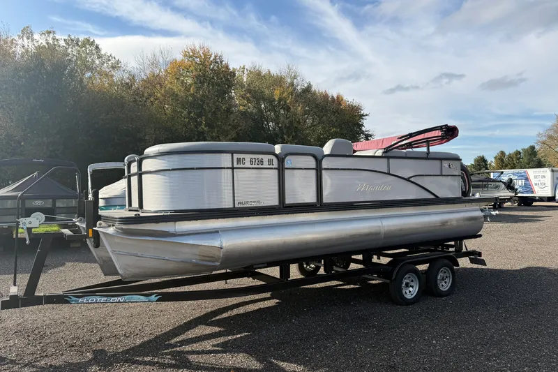 The Image of 2021 Manitou Aurora 21 pontoon boat on trailer, parked outdoors under a cloudy sky. - 0