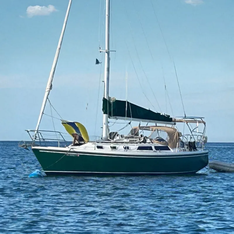The Image of A 1988 Catalina 34 sailboat rests calmly on the water, featuring a green sail and bimini. - 0