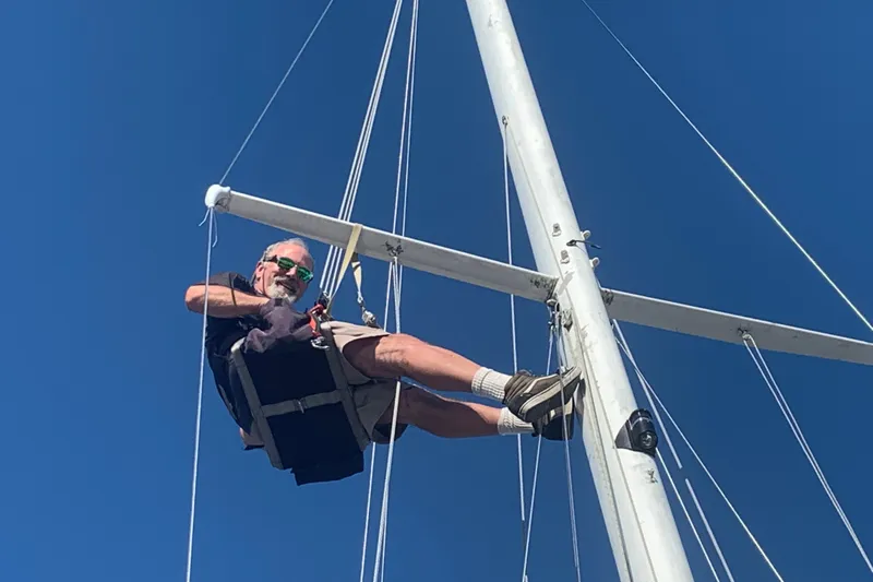 Slide: The Image of Man climbing mast of 1988 Catalina 34 sailboat under clear blue sky. - 52