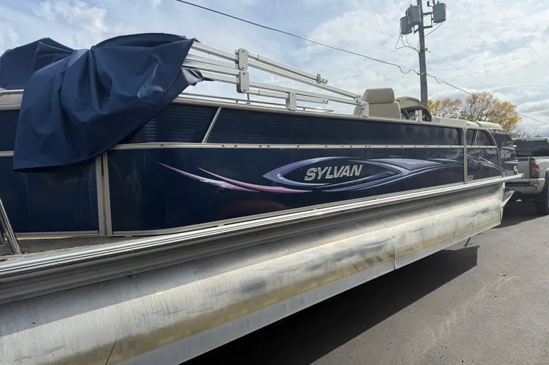 Slide: The Image of 2010 Sylvan 8525 Mandalay pontoon boat with blue cover, parked outdoors. - 7