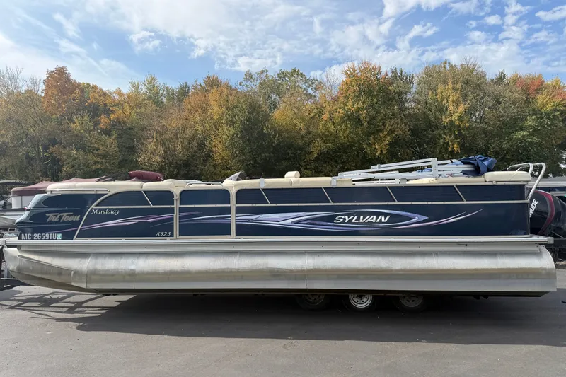 Slide: The Image of 2010 Sylvan 8525 Mandalay pontoon boat on trailer, surrounded by autumn trees. - 2