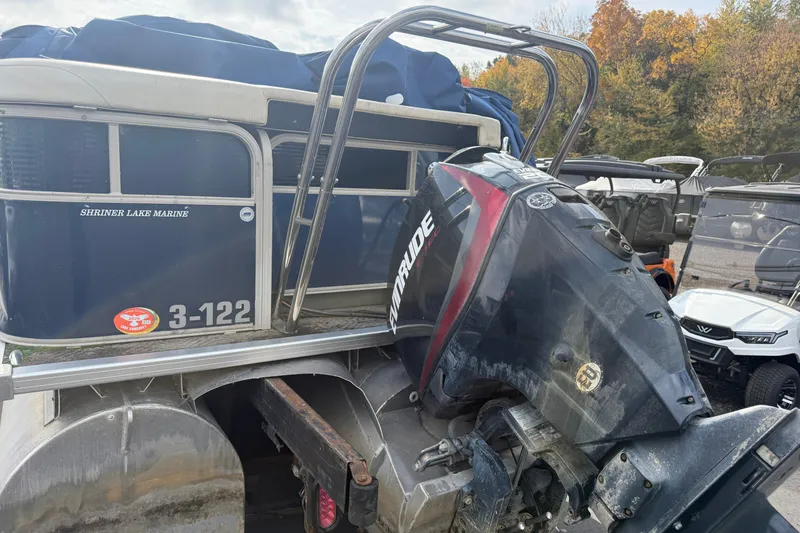Slide: The Image of 2010 Sylvan 8525 Mandalay boat with Evinrude motor, parked outdoors near autumn trees. - 1