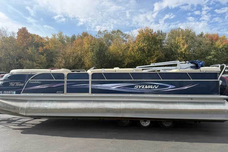 Slide: The Image of 2010 Sylvan 8525 Mandalay pontoon boat on trailer, surrounded by autumn trees. - 4