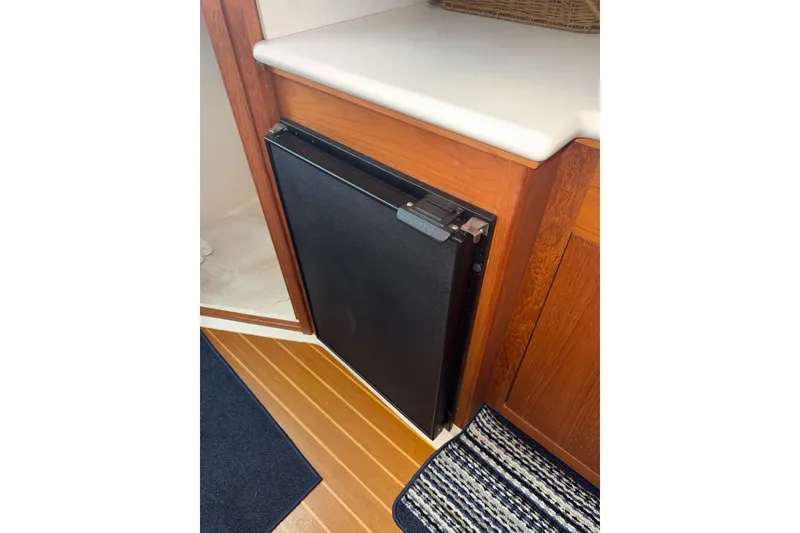 Slide: The Image of Compact refrigerator in 2002 Mainship Pilot 34 boat interior, featuring wood cabinetry and striped rug. - 17