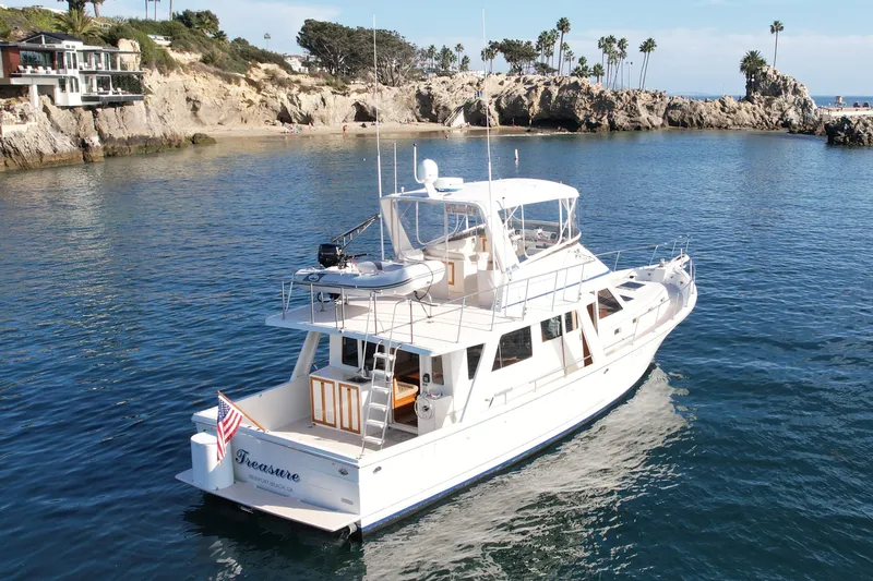 Slide: The Image of 1997 Offshore Yachts 48 Sedan cruising near rocky coastline with palm trees. - 10