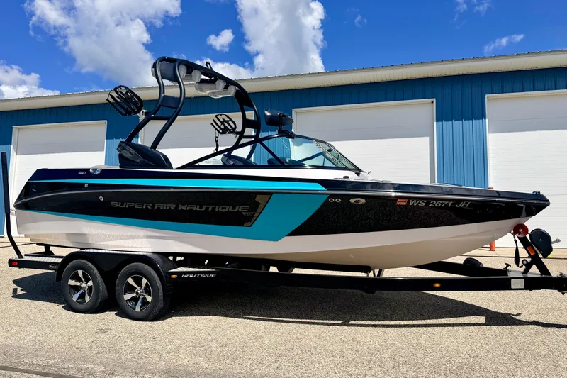 Slide: The Image of 2014 Nautique Super Air Nautique 210 boat on trailer, parked outside blue building. - 7