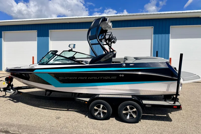 Slide: The Image of 2014 Nautique Super Air Nautique 210 boat on trailer, parked near blue building. - 5