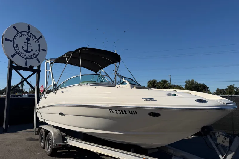The Image of 2006 Sea Ray 220 Sundeck boat on trailer at dealership under clear blue sky. - 0