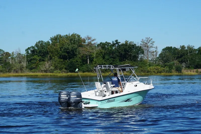 Slide: The Image of 2008 Angler 220WA boat cruising on a calm lake with lush green trees. - 2