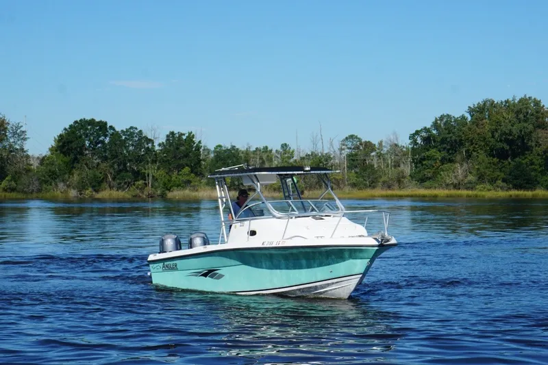 Slide: The Image of 2008 Angler 220WA boat cruising on a serene lake with lush green shoreline. - 5