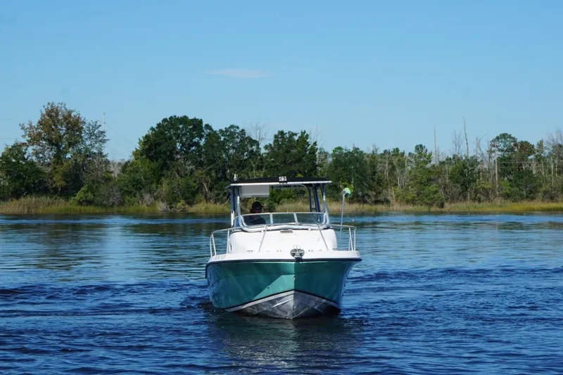 Slide: The Image of 2008 Angler 220WA boat cruising on a calm lake with forested shoreline. - 7