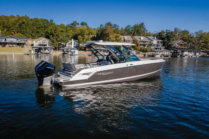 Slide: The Image of 2026 Monterey Elite 30 OB boat on a serene lake with waterfront homes. - 71