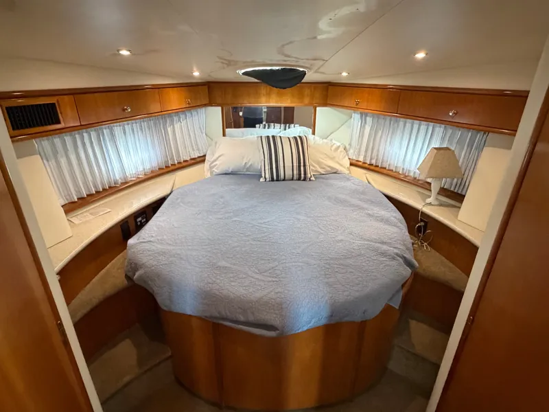 Slide: The Image of The cabin of the 2002 Carver 396 Aft Cabin Motor Yacht features a large bed with a blue cover, surrounded by wood furnishings and curtains. - 21