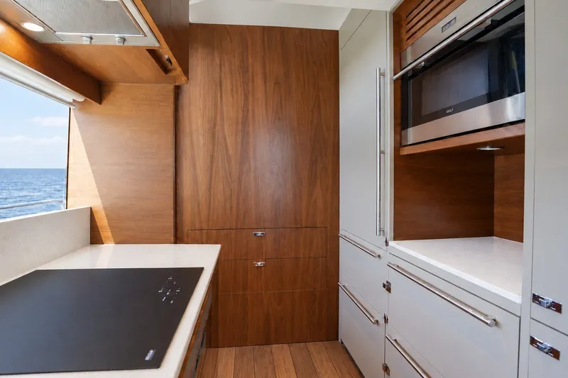 Slide: The Image of De keuken van de Princess Y85 uit 2021 heeft moderne houten panelen, een kookplaat en een ingebouwde oven. - 31
