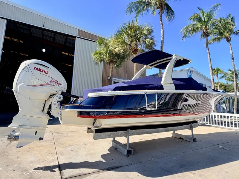 The Image of A 2019 Chris-Craft Launch 28 GT OB with Yamaha outboard motor, set on a stand near palm trees. - 0