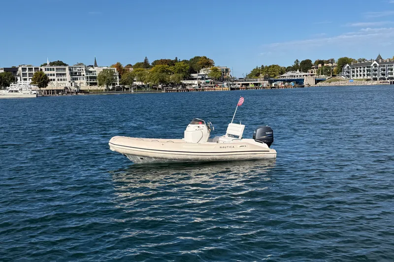 The Image of 2004 Nautica RIB 15 Widebody boat on calm water with scenic shoreline background. - 1